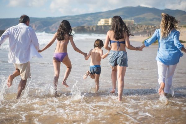 A family having fun running into the ocean on a sunny beach day in Portugal. Joyful and carefree moments.