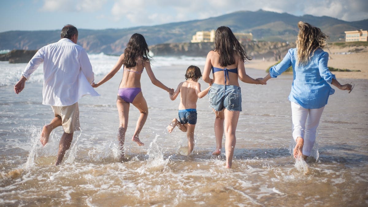 A family having fun running into the ocean on a sunny beach day in Portugal. Joyful and carefree moments.
